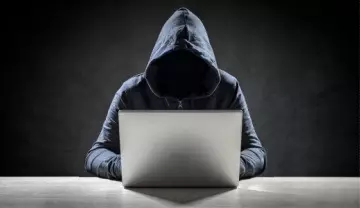 faceless man in a hoodie on a laptop