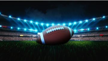 American football sitting on the field with stadium lights on