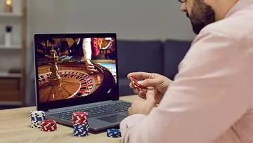 man playing online roulette on his laptop while holding casino chips