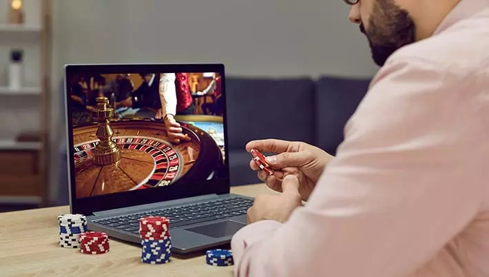 man playing online roulette on his laptop while holding casino chips