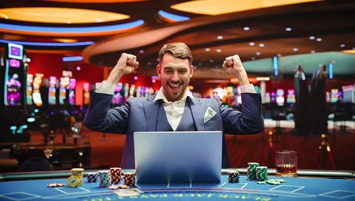 man celebrating with a laptop and a casino background