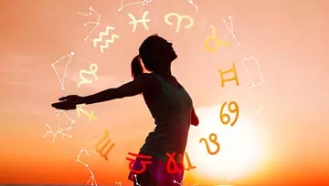 Woman standing on the beach at sunrise with zodiac symbols and star configurations around her