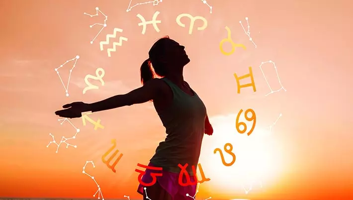 Woman standing on the beach at sunrise with zodiac symbols and star configurations around her