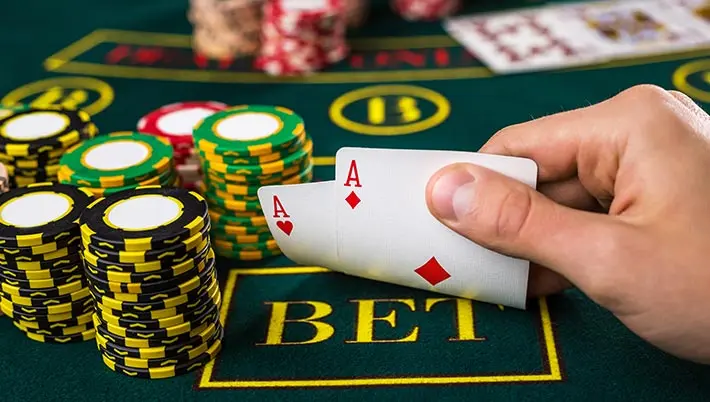 Man playing Texas Holdem showing us hiw pair of Aces next to piles of poker chips