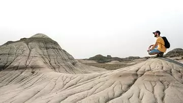 man standing next to sand dunes and dinosaur tracks