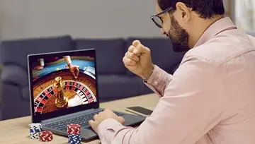 man looking at a screen with a roulette wheel, making a “winning” gesture