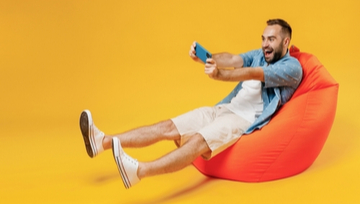 An excited young man sitting on a bean cushion playing mobile games 