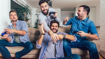 four guy friends excitedly playing video games each with his own console.