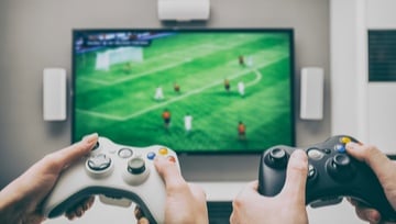 2 gamers using a controller to play soccer on TV