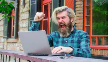 bearded man sitting outside with his laptop celebrating a video poker win