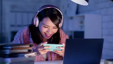 female gamer playing on her mobile with her laptop opened in front of her