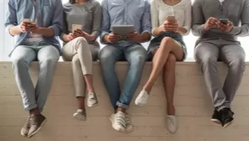 five friends sitting on a short wall playing on their phones