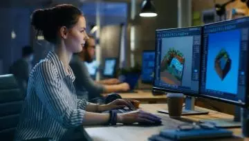 Woman game developer working on 2 computer screens 
