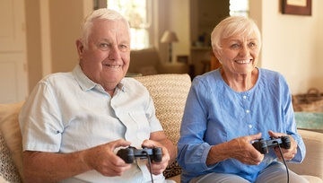 older couple sitting on their sofa each playing on a gaming device