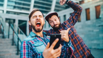 two friends outside a sports stadium ecstatic over a win on their phone
