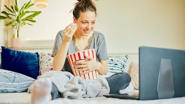 a woman enjoying a movie on her laptop sitting on her sofa eating popcorn